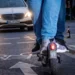 Rückansicht von zwei Personen, die sich einen E-Scooter auf einem Radweg mit Fahrradsymbol teilen, während sich im Hintergrund ein Taxi bei Dämmerung nähert.