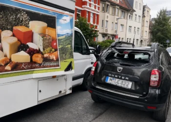 Geöffnete seitliche Verkaufsklappe eines Käse-Verkaufswagens ragt in die Fahrbahn, dahinter ein Dacia Duster mit zerbrochener Heckscheibe.