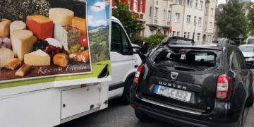 Geöffnete seitliche Verkaufsklappe eines Käse-Verkaufswagens ragt in die Fahrbahn, dahinter ein Dacia Duster mit zerbrochener Heckscheibe.