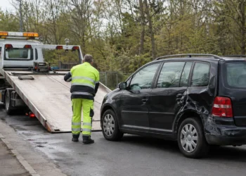 Mitarbeiter eines Abschleppdienstes in gelber Warnkleidung lädt einen beschädigten schwarzen Kombi auf einen Abschleppwagen.
