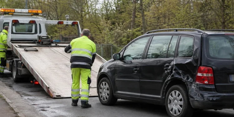 Mitarbeiter eines Abschleppdienstes in gelber Warnkleidung lädt einen beschädigten schwarzen Kombi auf einen Abschleppwagen.