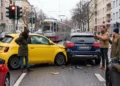 Frontalzusammenstoß zwischen einem gelben Kleinwagen und einem dunklen SUV an einer Straßenkreuzung, Beteiligte und Zeugen stehen daneben.