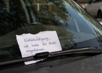 Handgeschriebener Zettel nach einem Parkrempler unter dem Scheibenwischer eines geparkten Autos, mit teilweise verdeckter und nicht lesbarer Telefonnummer