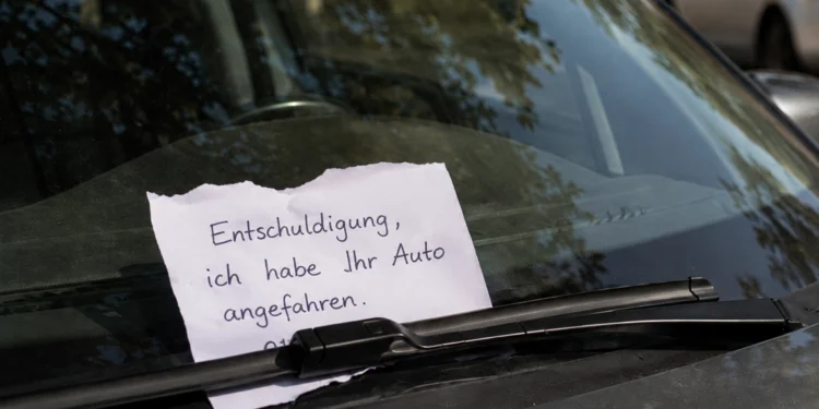 Handgeschriebener Zettel nach einem Parkrempler unter dem Scheibenwischer eines geparkten Autos, mit teilweise verdeckter und nicht lesbarer Telefonnummer