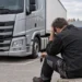 Berufskraftfahrer sitzt vor der Zugmaschine seines Lastwagens und stützt den Kopf in die Hand