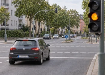 Dunkler Kompaktwagen rollt auf eine innerstädtische Kreuzung zu, die Ampel am rechten Fahrbahnrand zeigt Gelb.