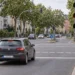 Dunkler Kompaktwagen rollt auf eine innerstädtische Kreuzung zu, die Ampel am rechten Fahrbahnrand zeigt Gelb.