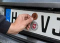 Hand befestigt eine braune HU-Plakette für 2026 auf einem Kennzeichen mit dem Kürzel H‑VJ, darunter das Niedersachsen-Siegel