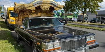 Schwarzer Cadillac Brougham mit vergoldetem japanischem Tempelaufbau auf dem Heck, abgestellt an einer Straße in einem Gewerbegebiet.