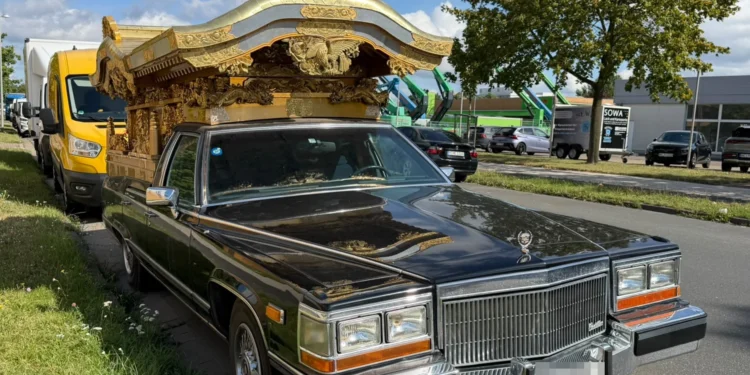 Schwarzer Cadillac Brougham mit vergoldetem japanischem Tempelaufbau auf dem Heck, abgestellt an einer Straße in einem Gewerbegebiet.