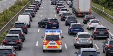 Stau auf einer dreispurigen Autobahn: Zwischen der linken und den übrigen Fahrspuren ist eine Rettungsgasse frei, durch die ein Einsatzfahrzeug mit Blaulicht fährt.