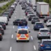 Stau auf einer dreispurigen Autobahn: Zwischen der linken und den übrigen Fahrspuren ist eine Rettungsgasse frei, durch die ein Einsatzfahrzeug mit Blaulicht fährt.