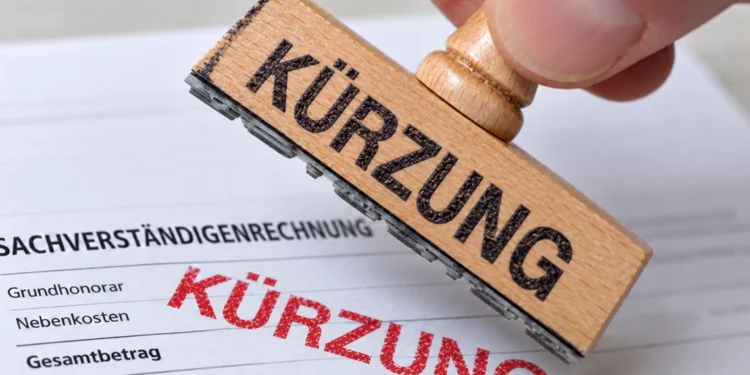 Hand mit einem Holzstempel, der das Wort Kürzung rot auf eine Sachverständigenrechnung druckt