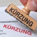 Hand mit einem Holzstempel, der das Wort Kürzung rot auf eine Sachverständigenrechnung druckt