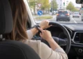 Fahrerin am Lenkrad tippt während der Fahrt auf ihre Smartwatch, im Hintergrund eine Kreuzung im Stadtverkehr