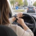 Fahrerin am Lenkrad tippt während der Fahrt auf ihre Smartwatch, im Hintergrund eine Kreuzung im Stadtverkehr