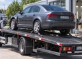Grauer Pkw mit Frontschaden auf der Ladefläche eines Abschleppwagens vor einer Kfz-Werkstatt