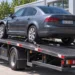 Grauer Pkw mit Frontschaden auf der Ladefläche eines Abschleppwagens vor einer Kfz-Werkstatt