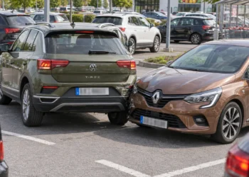 Auf einem Supermarktparkplatz ist ein grüner SUV beim Ausparken mit der Front eines braunen Kleinwagens zusammengestoßen, im Hintergrund Einkaufswagen und weitere geparkte Autos.