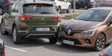 Auf einem Supermarktparkplatz ist ein grüner SUV beim Ausparken mit der Front eines braunen Kleinwagens zusammengestoßen, im Hintergrund Einkaufswagen und weitere geparkte Autos.
