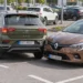 Auf einem Supermarktparkplatz ist ein grüner SUV beim Ausparken mit der Front eines braunen Kleinwagens zusammengestoßen, im Hintergrund Einkaufswagen und weitere geparkte Autos.